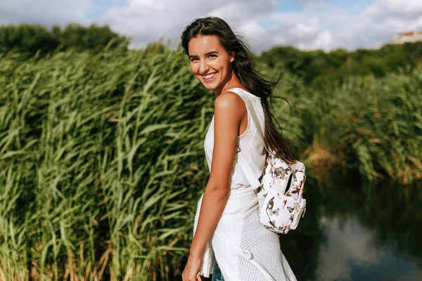 Horizontal imagem de feliz bela jovem morena sorrindo e olhando tot ele câmera com um vento soprando cabelos longos no parque . — Fotografia de Stock