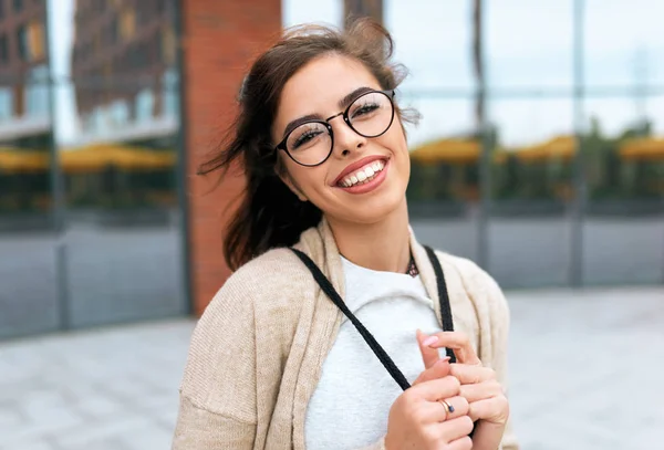 Ao ar livre retrato de estudante muito jovem sorrindo amplamente com sorriso de dente, com mochila nas costas, vestindo óculos transparentes olhando para a câmera, posando na rua da cidade . — Fotografia de Stock