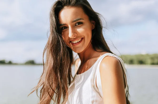 Güzel mutlu genç bir kadının açık hava portresi. Dişli bir gülümsemeyle, rüzgarlı uzun saçlarıyla parkta, doğa arka planında poz veriyor.. — Stok fotoğraf