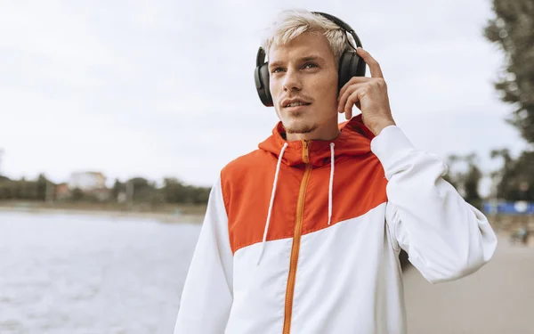 Привабливий молодий чоловік слухає свою улюблену музику з бездротових навушників за допомогою смартфона під час ходьби в парку . — стокове фото