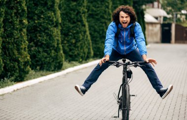 Bisiklet sürerken sokakta gülümseyen mutlu bir adamın açık havada çekilmiş görüntüsü. Kıvırcık saçlı neşeli erkek kurye şehirde bisikletli paket teslim ediyor..