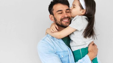 Kapalı alanda gülümseyen bir baba imajı. Güzeller güzeli kızının yanaktan öpüşmesini kucakla. Babasını ve küçük kızını sevmek, kucaklaşmak ve birlikte eğlenmek. Çocukluk ve babalık kavramı