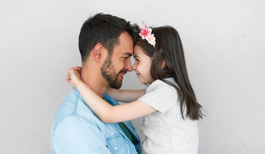 Horizontal studio portrait of happy father smiling, embracing his cute daughter, and looking at each other. Loving daddy and his little girl cuddling and enjoying time together on Father's Day.