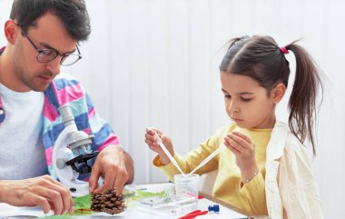 Babası ve kızı mikroskopla çalışıyor ve araştırıyorlar. Baba ve küçük kız kimya dersini mikroskopla inceleyip laboratuvar deneyleri için şişelerde sıvıları karıştırıyorlar. Evde eğitim kavramı.
