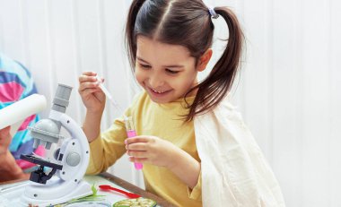 İçeride, babasıyla laboratuarda bilimsel deneyler yapan gülümseyen küçük bir kızın görüntüsü. Baba ve kızı mikroskopla biyoloji ve kimya dersi alıyor. Evde eğitim ve eğitim kavramı.