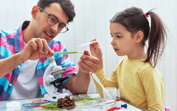 Yakışıklı baba ve tatlı kız, biyoloji ve kimya derslerini mikroskopla inceliyor. Babası olan küçük bir kız laboratuarda yaprak üzerinde bilimsel deneyler yapıyor. Evde eğitim ve eğitim kavramı.