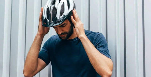 Professional cyclist wears the protective helmet and thinking about the route for triathlon outdoor. Male athlete preparing before the riding the bike outside.