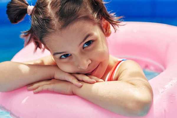 夏休みにプールに浮かぶインフレータブルピンクのリングでリラックスしたカラフルな水着でかわいい子供のイメージを閉じます 幸せな女の子横たわっインフレータブルサークルでザプール — ストック写真