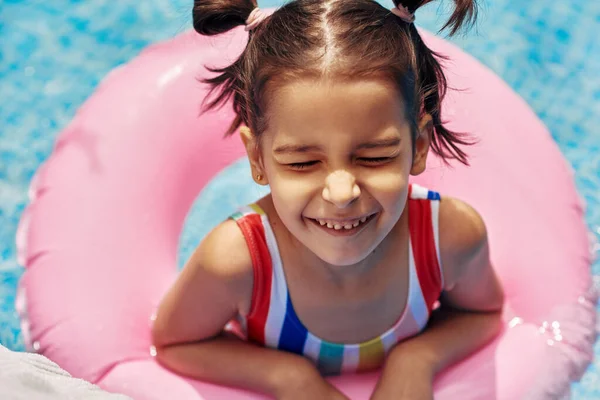 在暑假期间 穿着五颜六色泳衣的孩子在游泳池里漂浮着一个充气粉红环上放松的形象 快乐的小女孩躺在游泳池里一个充气的圆圈上 — 图库照片