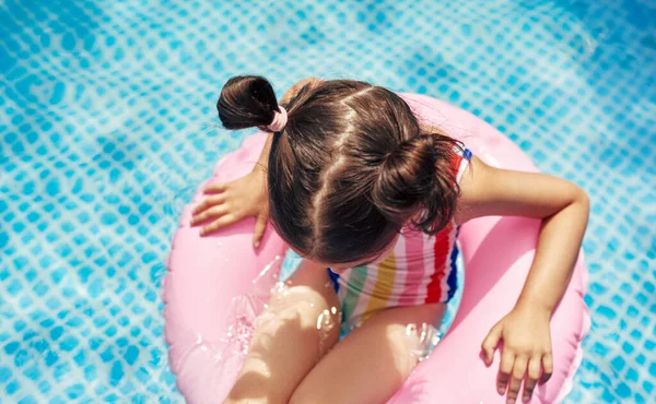 从上面看一个穿着五颜六色泳衣的可爱的孩子在夏天的假期里在游泳池里漂浮着一个充气的粉色环上放松 漂亮的小女孩坐在游泳池的充气圆圈上 — 图库照片