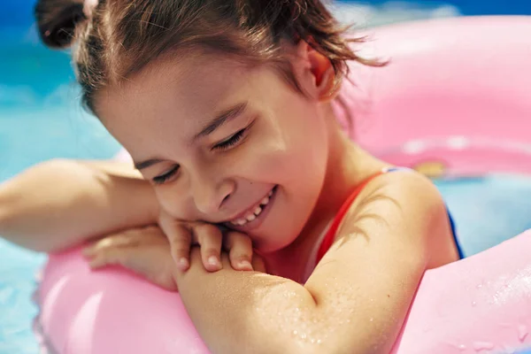 아름다운 소녀가 여름휴가 연못에 부풀어 오르는 분홍색 반지를 쉬면서 미소짓는다 — 스톡 사진