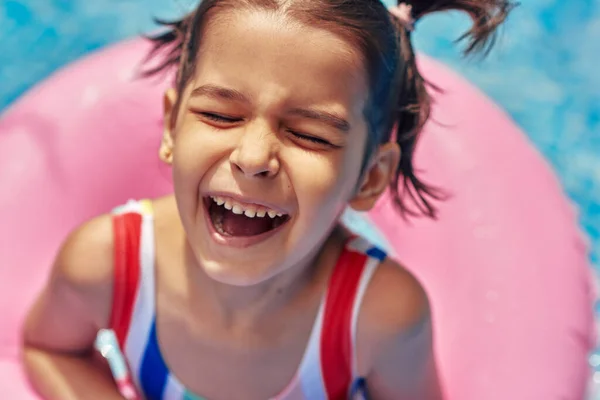 一个穿着五颜六色泳衣的快乐的孩子在一个充气的粉色戒指上玩耍 在一个游泳池里度过暑假的场景 微笑的小女孩在游泳池的充气圆圈上放松 — 图库照片