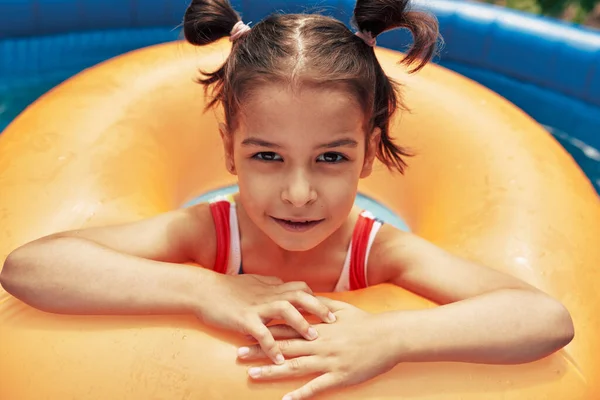 夏休みにプールに浮かぶ膨脹可能なオレンジ色のリングでリラックスしたカラフルな水着のかわいい子供の屋外肖像画 スイミングプールでインフレータブルサークルで遊んでいる女の子 — ストック写真