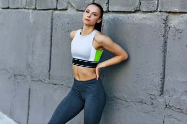 Spor yaptıktan sonra gri Cocnnet duvarının yanında poz veren çekici genç bir kadın. İnce bir kadın sabah egzersizden sonra dinleniyor..