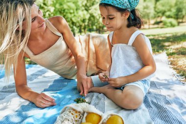 Çekici, gülümseyen anne ve kızı parkta çimlerin üzerinde oturmuş limonlarla oynuyorlar. Kadın ve çocuğu yaz pikniği yapıyorlar. Anneler Günü konsepti.