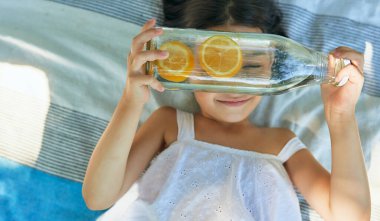 Parktaki bir piknik sırasında cam şişesinde limonatayla battaniyenin üzerine uzanmış şirin küçük bir kızın manzarası. Çocuk ailesiyle yaz pikniği yapıyor. Çocuk dışarıda dinleniyor..