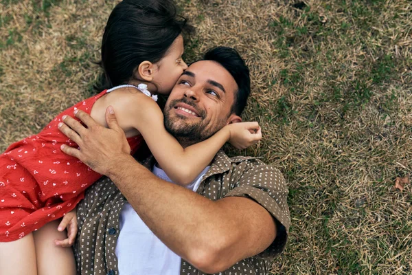 Bir babanın piknik sırasında dışarıda çimlerin üzerinde kızına sarılmasının en güzel görüntüsü. Babam çocuğuyla gün içinde parkta eğleniyor. Babalar Günün kutlu olsun. Baba ve kızı sevgilerini paylaşıyor..