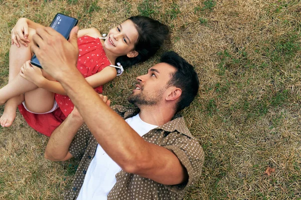 Ojciec Bawi Się Córką Smartfonie Podczas Relaksu Trawie Świeżym Powietrzu — Zdjęcie stockowe