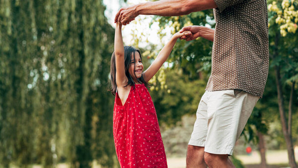 На улице горизонтальное изображение маленькой девочки, танцующей со своим отцом в парке. Дочь играла со своим любящим папой на природе. Папа и ребенок веселятся. 