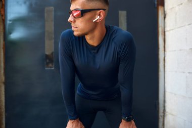 Atletizm sporcusu dizlerinin üzerine çöküp kafasını çevirmiş şehirdeki metal duvarlara bakıyor. Dışarıdaki caddede koştuktan sonra dinlenen sağlıklı bir erkek..