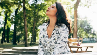 Güzel bir genç kadının yatay görüntüsü, gökyüzüne bakarken rüya gibi bir yüz ifadesi var. Güneşli bir günde parkta dinlenen güzel kız..