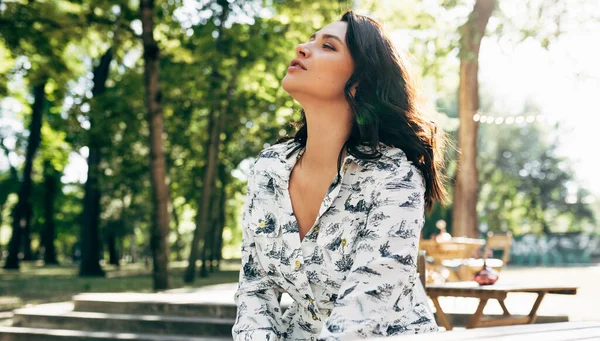 Güzel bir genç kadının yatay görüntüsü, gökyüzüne bakarken rüya gibi bir yüz ifadesi var. Güneşli bir günde parkta dinlenen güzel kız..