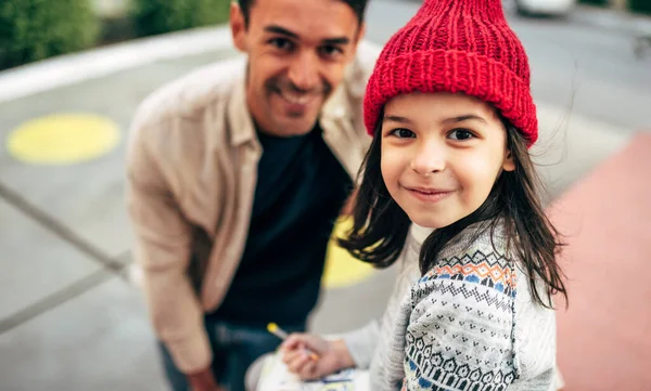 모자를 귀여운 소녀가 야외에 아버지와 그림을 그리고 있습니다 아버지는 밖에서 — 스톡 사진