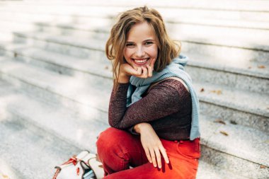 Neşeli kız öğrenci geniş bir gülümsemeyle kameraya bakıyor, güneşli bir günde kampüsün yanında oturuyor. Sıradan kıyafetli güzel sarışın bir kadın sokakta dinleniyor..