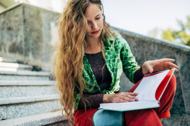 Güneşli bir günde üniversite kampüsünün merdivenlerinde oturmuş kitap okuyan güzel bir kız öğrenci. Sıradan kıyafetli güzel bir kadın dışarıda dinleniyor ve bir kitaptan öğreniyor..