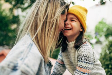 Sarı şapkalı mutlu küçük kızın portresi mavi kot ceketli annesine sarılıyor. Annesini kucaklayan sevimli çocuk dışarıda eğleniyor. Anne ve kızı sevgiyi paylaşıyor. Anneler Günü.