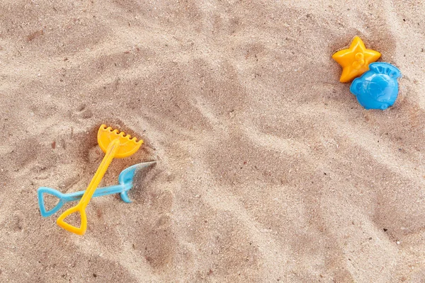 Bright plastic childrens toys in the sand. Concept of beach recreation for children. Childrens summer games. Summer concept. Flat lay, top view, copy space, blue and yellow.