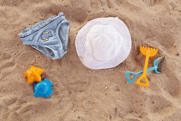 Plaj aksesuarları çocuklar düz için yatıyordu. Kum üzerinde üstten görünüm çocuk plaj öğeleri. Bebek plastik kaşık, Komisyon, şapka ve mavi çocuk külot. Su oyuncakları. Aile yaz tatil tropikal tatil.