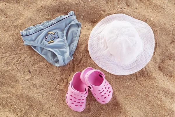 Baba nyári fürdőruha, pink flip papucs, fehér kalapot, bugyik a kék hal, a homokos strand. Holiday koncepció. Gyermek és a család hivatása. — Stock Fotó
