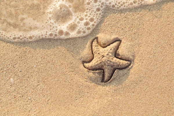 Морская звезда, нарисованная на песке, смывается волной. Пенящаяся морская волна идет мыть картину на мокром желтом пляжном песке. Праздничное и призвание. Вид сверху. Копирование пространства . — стоковое фото
