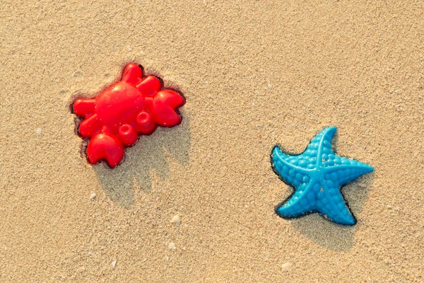 Plastic colored shapes for children play with sand on the beach. Baby plastic molds lying in the sand on the seabeach. Two bright summer toys - red crab and blue starfish in the sand in sunny day. — Stock Photo, Image