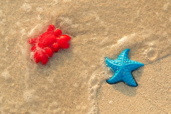 Красочные игрушки на берегу моря. Красный краб и голубая морская звезда смыты морской волной . — стоковое фото