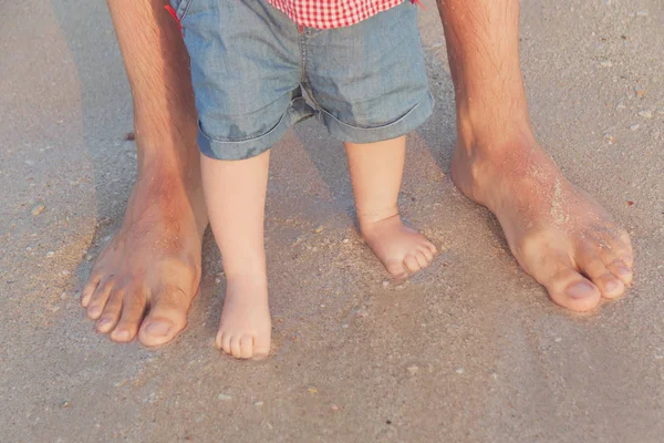 Man and baby feet standing in shallow water waiting for the wave. Bare feet father and his little daughter or son staying in the sand near the sea. Concept of travel and holidays. Toned. Soft focus