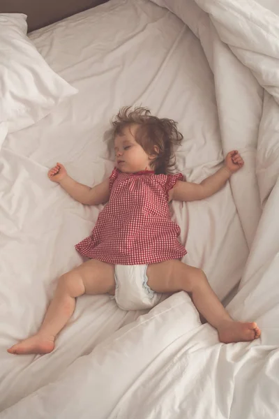 Kollarını açarak ve emzik beyaz çarşaflı yatakta olmadan sırt üstü uyuyan kız bebek. Aydınlık bir salonda uyuyan huzurlu. Tam yükseklik, dikey. Retro pastel tonda. Yumuşak odak
