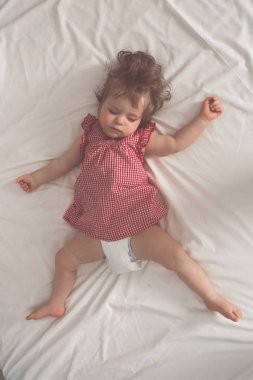 Kollarını açarak ve emzik beyaz çarşaflı yatakta olmadan sırt üstü uyuyan kız bebek. Aydınlık bir salonda uyuyan huzurlu. Retro pastel tonda. Yumuşak odak