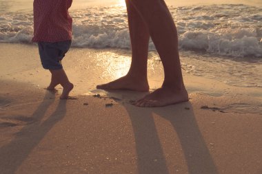 Baba, onun bebeği ile ilk adımlar yardım kavramı, açık samimi fotoğraf sahilde yürümeyi öğretim bebek bir gün plajda, sağlıklı aile yaşam harcamaları.