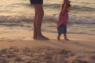 Baba, onun bebeği ile ilk adımlar yardım kavramı, açık samimi fotoğraf sahilde yürümeyi öğretim bebek bir gün plajda, sağlıklı aile yaşam harcamaları.