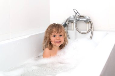 Eğlenceli neşeli mutlu toddler bebek köpük kabarcıkları ile oynarken bir banyo. Küçük çocuk bir küvet içinde. Banyo beyaz arka plan üzerinde gülümseyen çocuk. Bebek yıkama ve banyo. Hijyen ve sağlık.