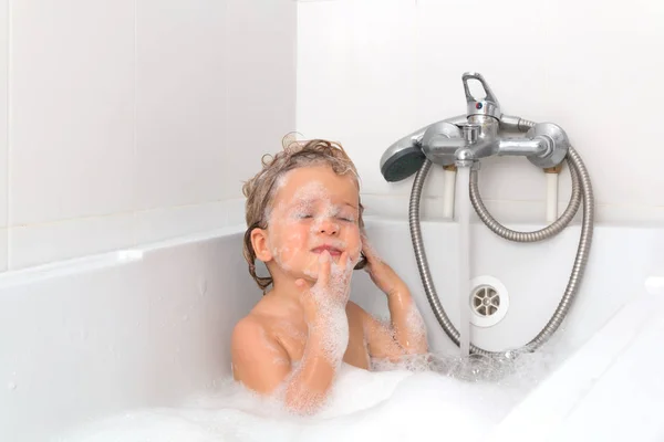 Küçük sarışın kız banyoda yüzünde köpükle. Gözler kapalı. Bağımsız bebek beyaz arka plan üzerinde banyo. Bebek yıkama ve banyo. Hijyen ve sağlık.