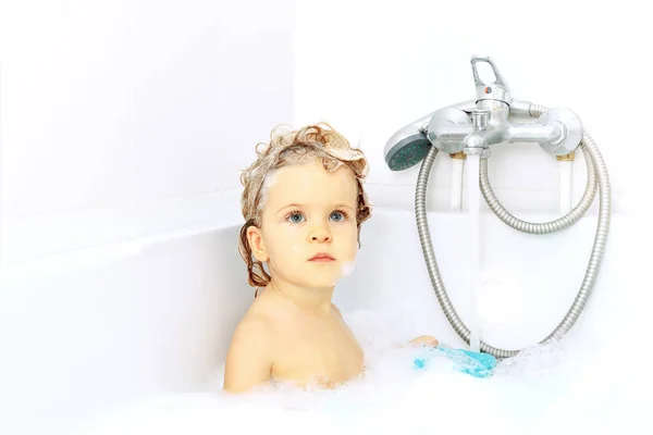 Şirin bebek alarak banyo lavabo su dokunun zemin üzerine yıkama içinde. Büyük mavi gözlü eğleniyor ve sabun köpüğü ile oynarken küçük sağlıklı kız. Ciddi görünümlü. Elinde oyuncak