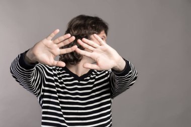 Çizgili kazaklı adam bir yana, ellerini ileriye uzanan döner. Birinden kişi bastırıyor. Yapma dur el işareti palm hareketi gri arka plan üzerinde adam. Uzak dur ve kavram dokunma bana