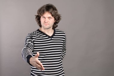 Siyah ve beyaz çizgili kazaklı ciddi bir adam, elinde bir el sıkışma samimiyet bir iş anlaşması mühürleme, tebrik veya tebrik gri arka plan üzerinde sunan bir işareti olarak sunar.