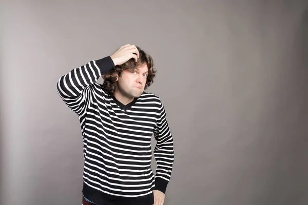 Puzzled guy with messy hair, frowning and looking unsatisfied scratching head, thinking deeply about something on grey wall background. Human facial expression, emotion, feeling, sign body language — Stock Photo, Image