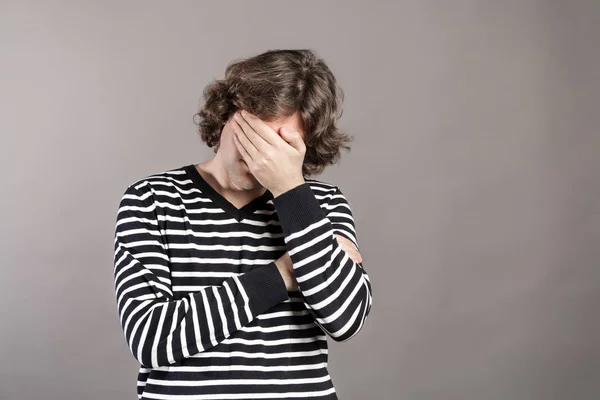 Portrait of upset man covering his face with hand isolated on grey background. Facepalm facial expression. Disappointed young shaved shaggy man covering his face with his hand. Negative emotions.
