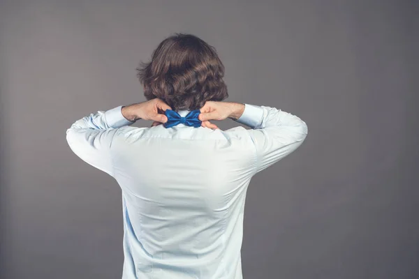 Señor. Perfecto. Vista trasera de un joven guapo con camisa azul ajustando su pajarita mientras está de pie sobre un fondo gris. Un tipo elegante y vestido. Tonificado. Copiar espacio . — Foto de Stock