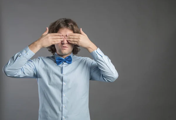 Man covering his eyes with hands on gray background. Shy male closing eyes by hands can\'t see hiding, wall background. See no evil concept. Negative human emotion, facial expression, feeling reaction.